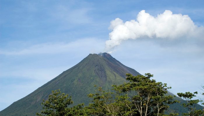 Panoramic view of Arenal volcano, in Alajuela, Costa Rica. Smoke comming out of the crater. No people, sunny day. The volcano was dormant for hundreds of years and exhibited a single crater at its summit, with minor fumaroles activity, covered by dense vegetation. In 1968 it erupted unexpectedly, destroying the small town of Tabacón. Due to the eruption three more craters were created on the western flanks but only one of them still exists today. Since 2010, Arenal has been dormant.